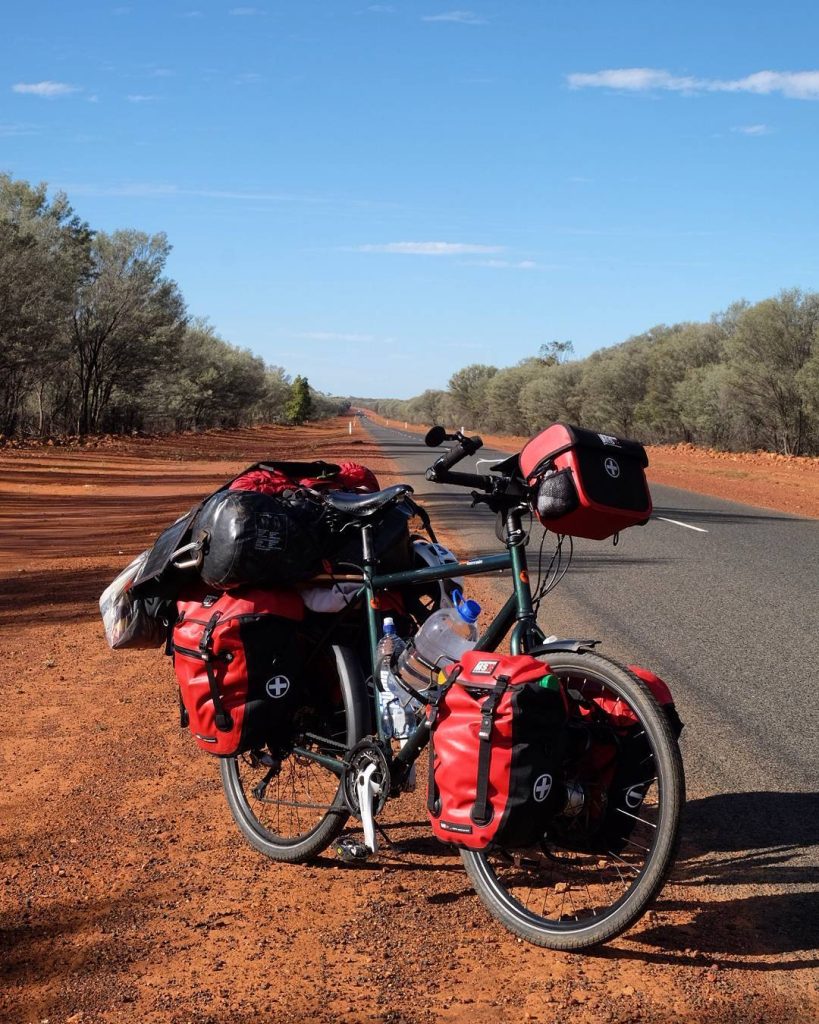 Vélo de voyage aux sacoches rouges sur une route de l'outback